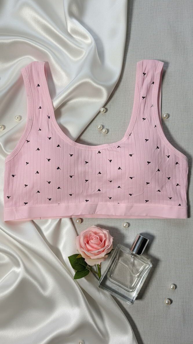 Pink ribbed bralette with black heart patterns on a textured surface with a rose and perfume bottle.