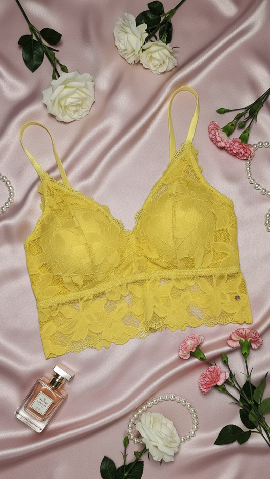 Yellow lace bralette on a pink satin background with flowers and jewelry.